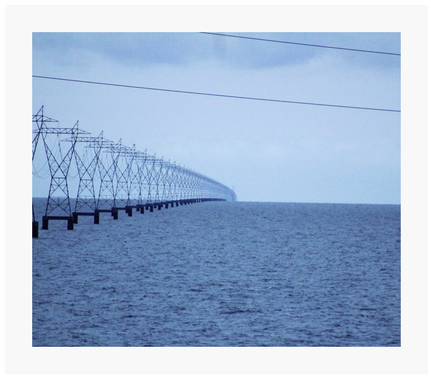 Pylons in the sea, repeating on and on. The pylons bend downwards as they go towards the horizon.